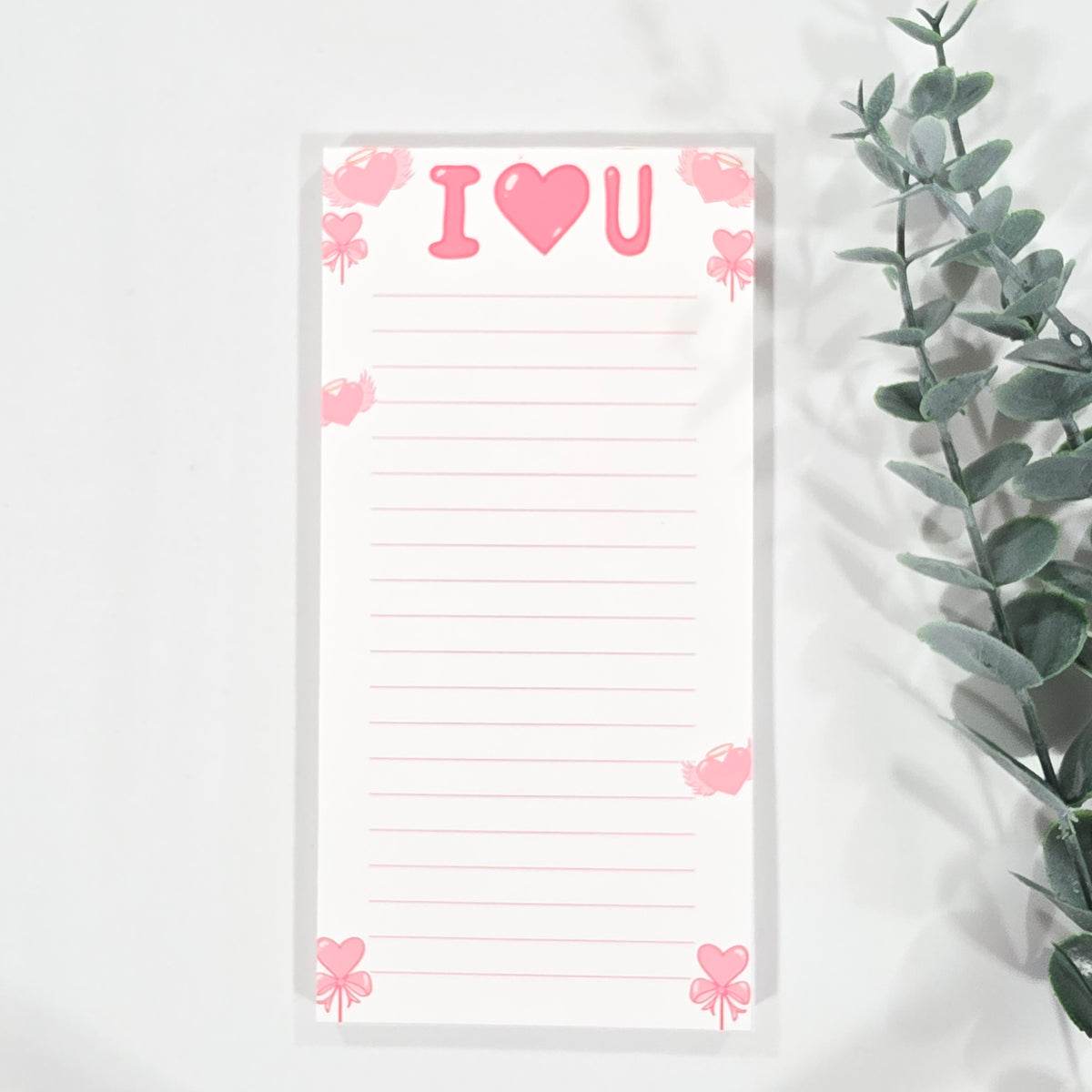 Notepad with 'I love you' text and pink heart design on a white background with green leaves.