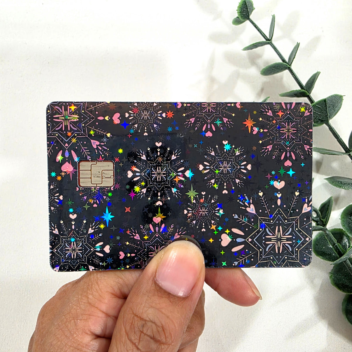 Card with colorful black and pink pattern held by a hand against a white background with green leaves.