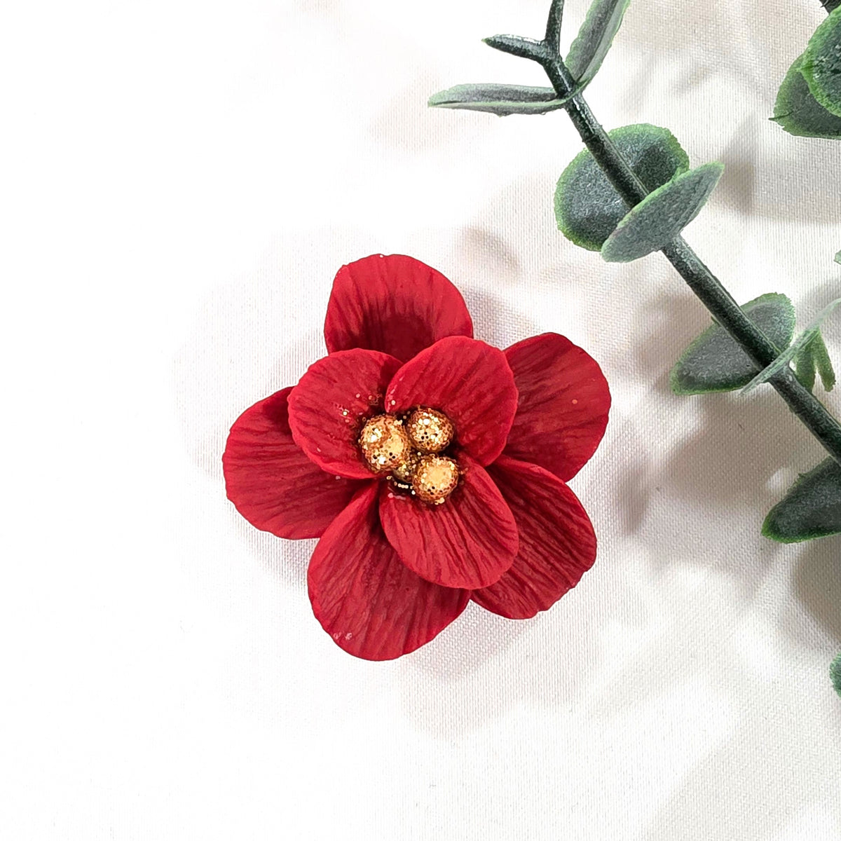 Red flower-shaped magnet with gold center on a white background