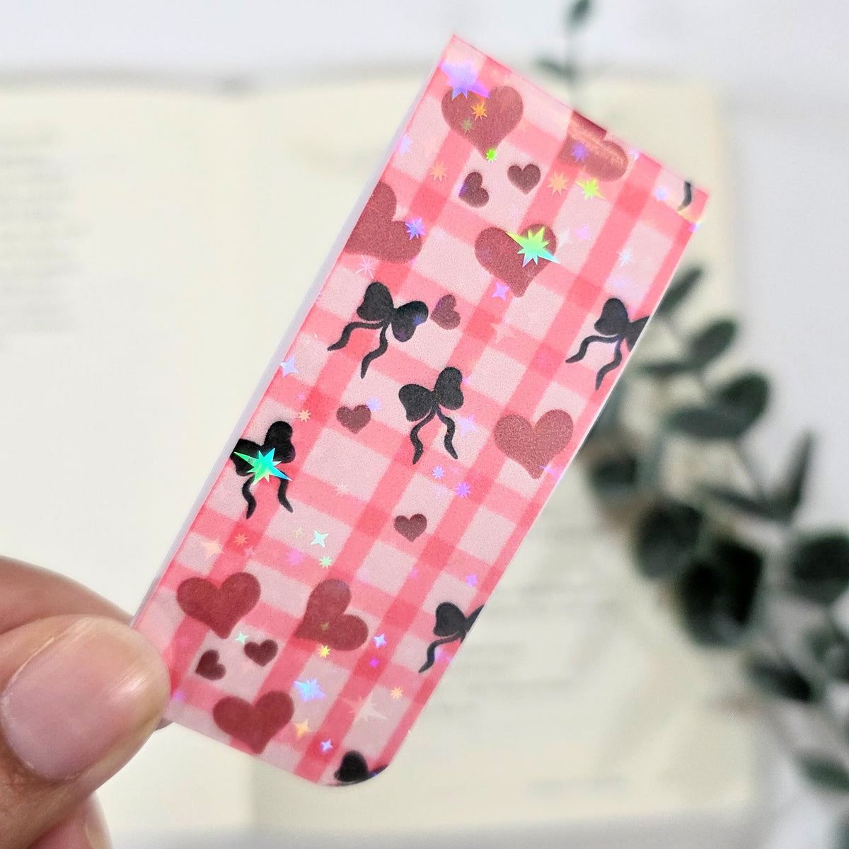 Pink checkered bookmark with heart and bow patterns held by a hand