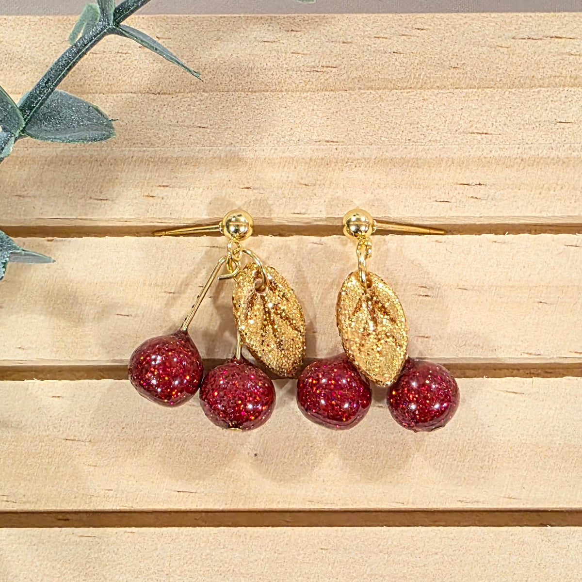 Gold earring with red polymer clay cherries on a wooden background