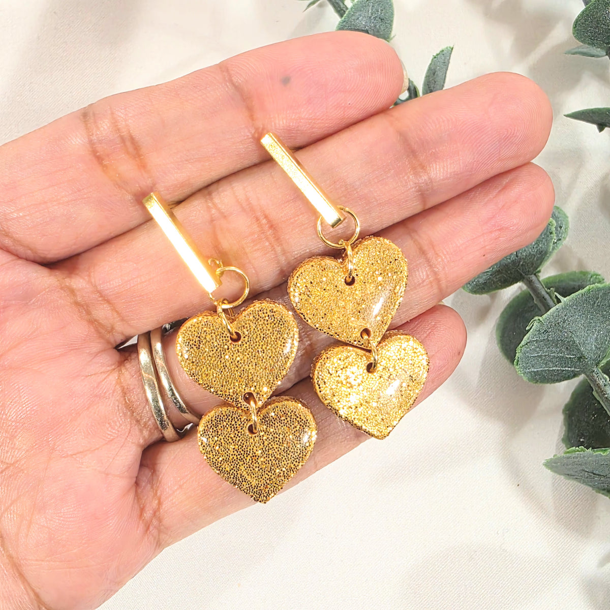 Gold heart-shaped earrings held in a hand with a light background