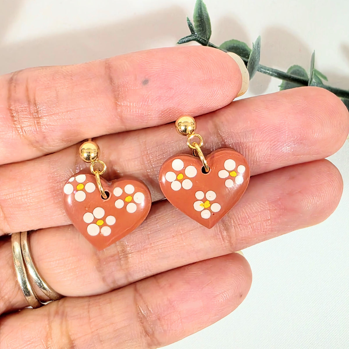 Heart-shaped earrings with floral design held between fingers