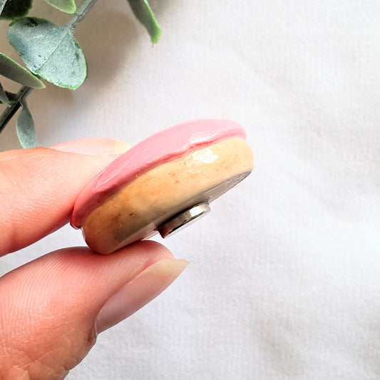 Hand holding a round magnet with pink and beige colors on a white background