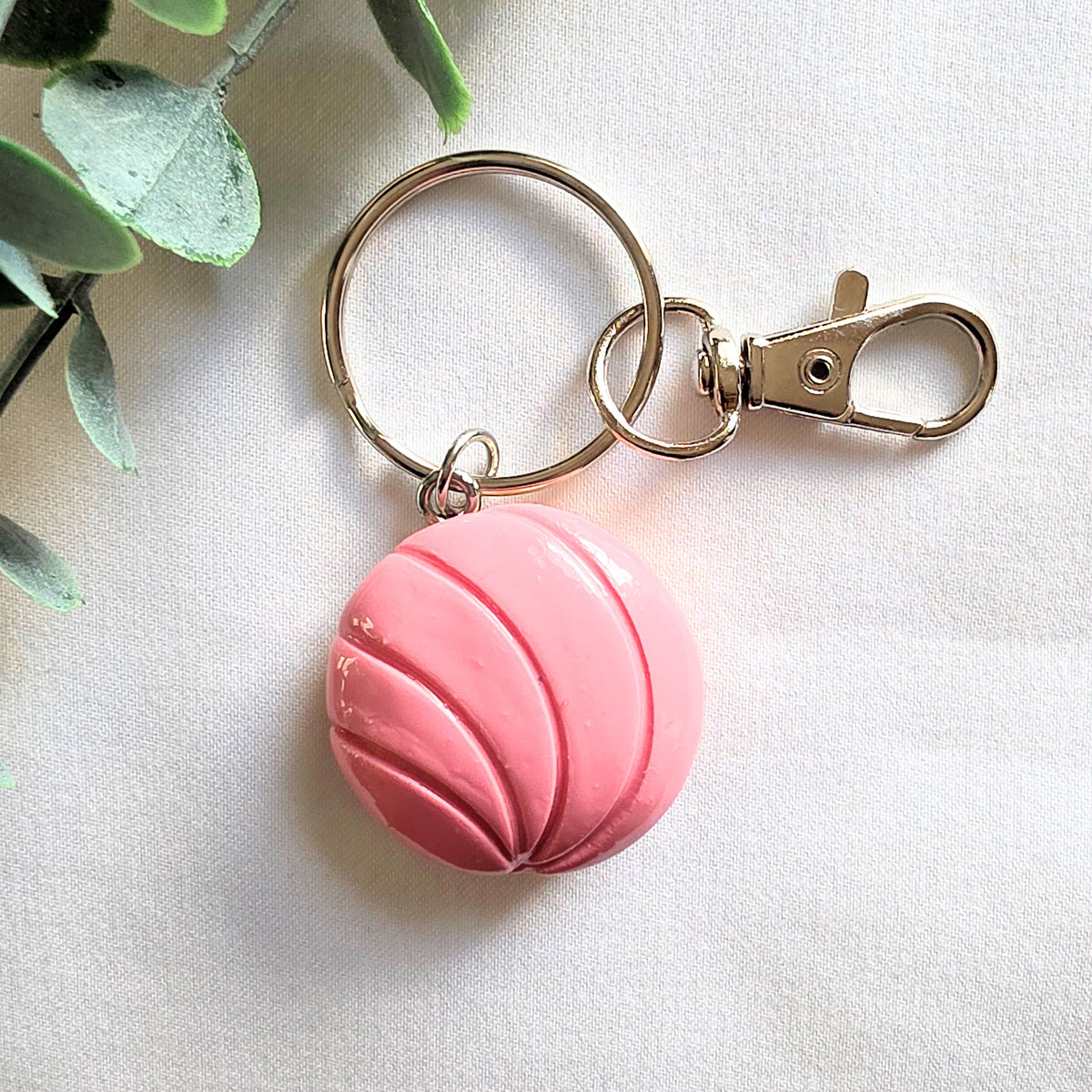 Pink conchita bread keychain with a gold clasp on a light background