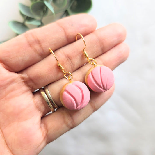 Pink earrings with gold hooks held in a hand against a blurred background