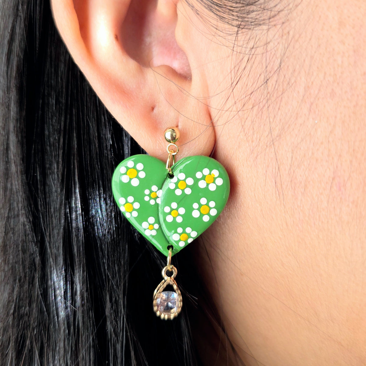 Green heart-shaped earrings with floral design worn by a person