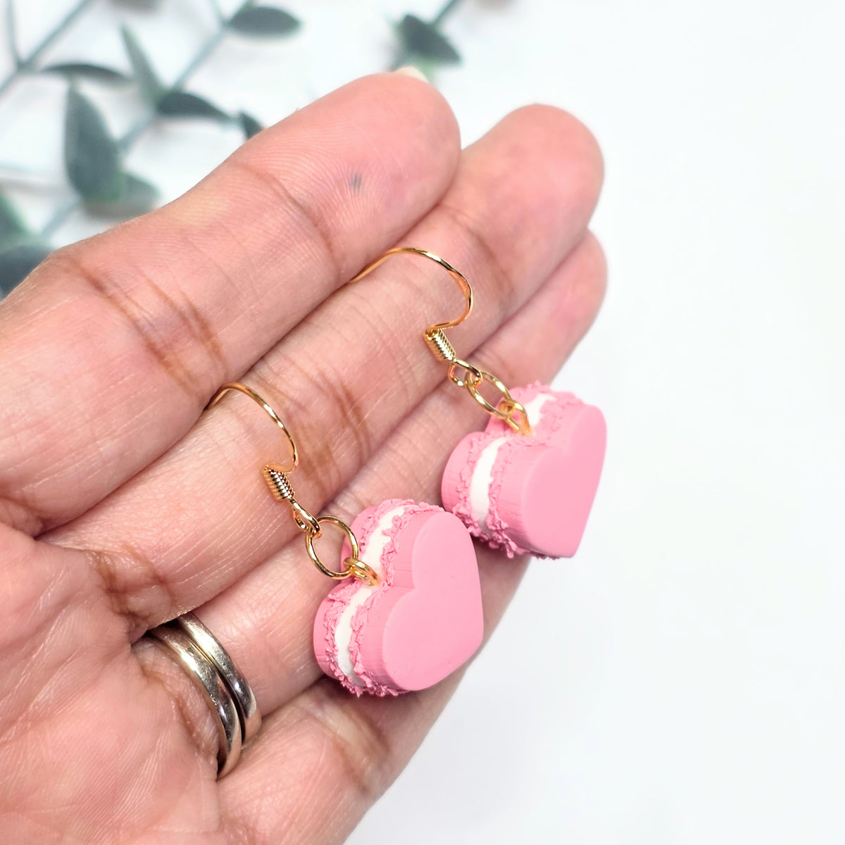 Pink macaron-shaped earrings on a hand with a blurred background