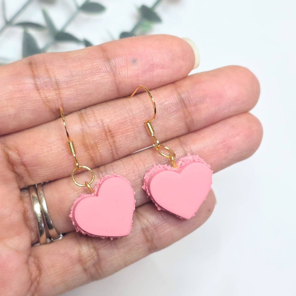 Pink heart-shaped earrings held in a hand with a blurred background