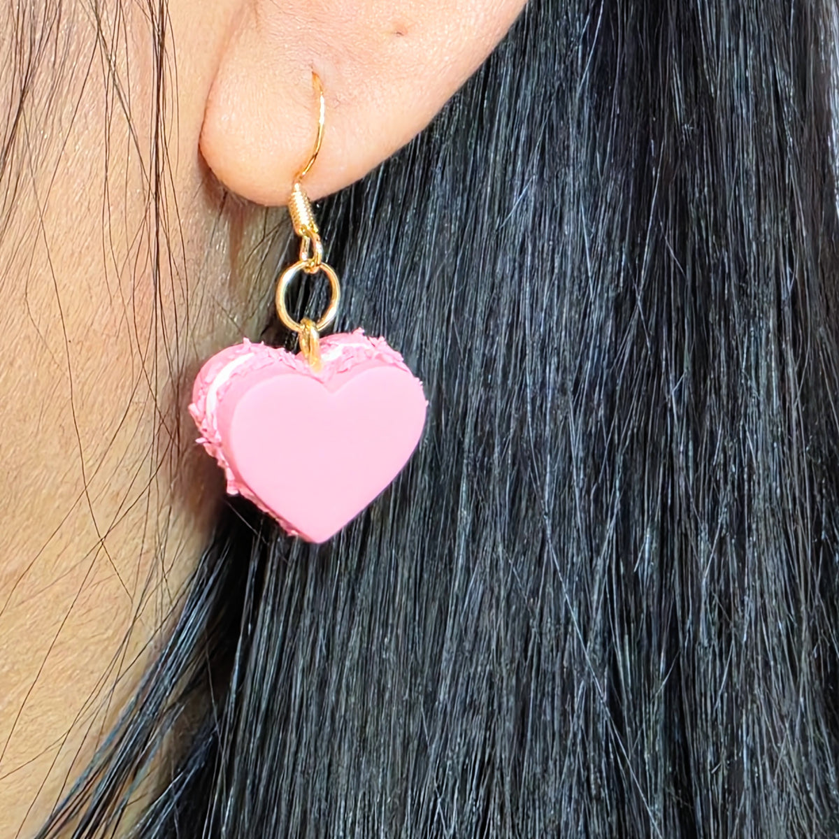 Pink heart-shaped earring worn by a person with dark hair.