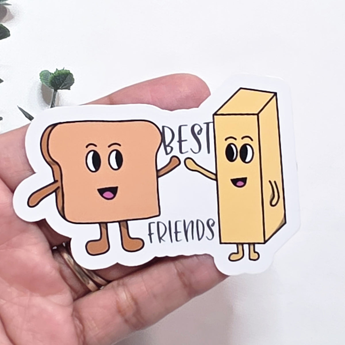 Sticker of a loaf of bread and a box with 'Best Friends' text held by a hand.