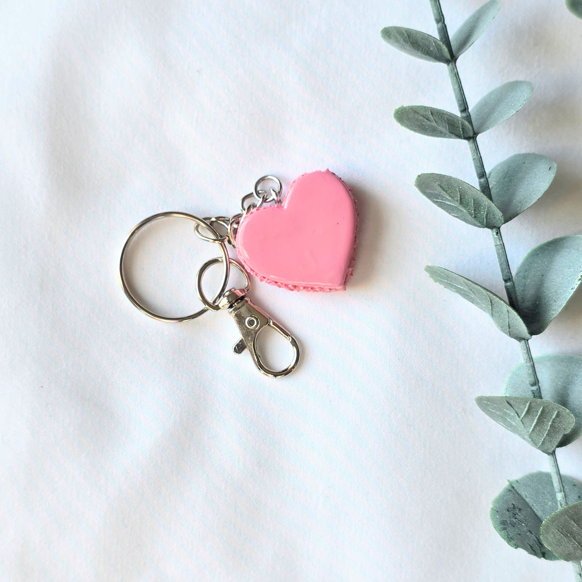 Pink heart-shaped keychain on a white background with a green leafy branch.