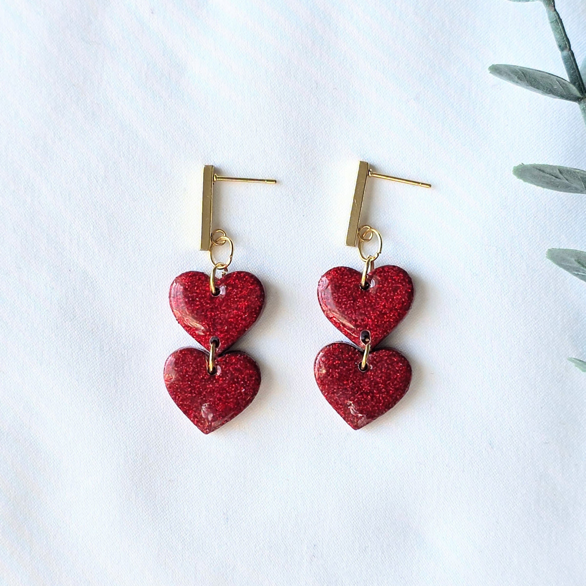 Red heart-shaped earrings on a white background with a plant leaf.