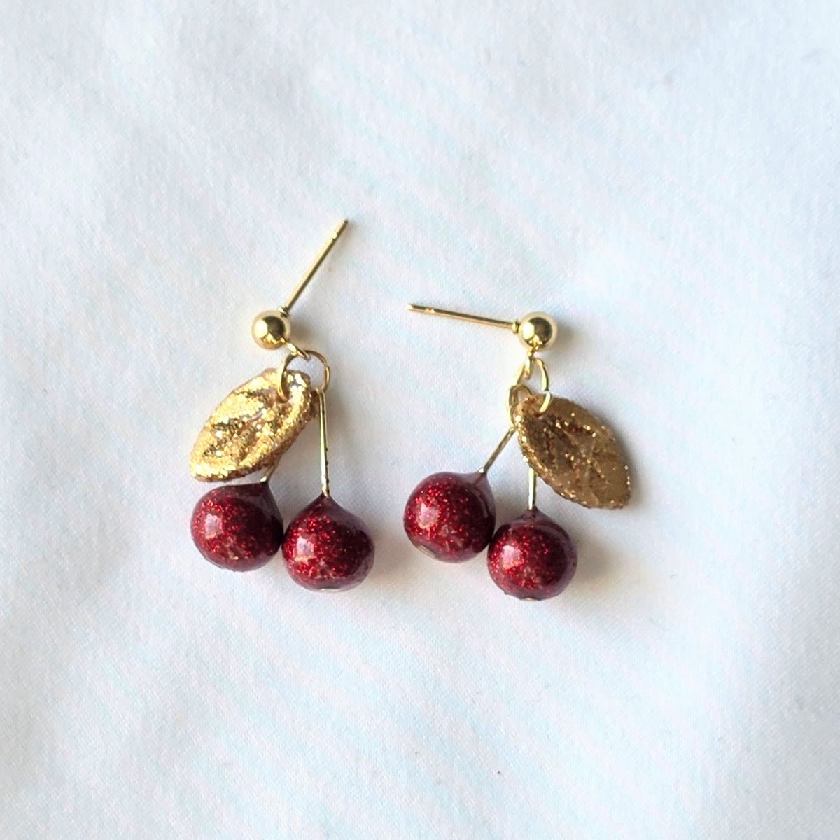 Cherry-themed earrings with gold leaves on a white background