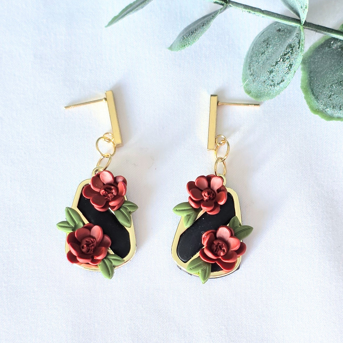 Pair of floral earrings on a white background with green leaves.