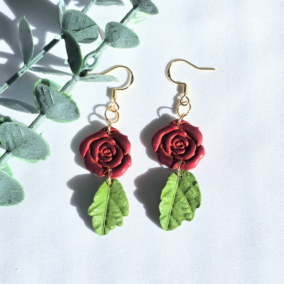 Red rose earrings with green leaves on a white background