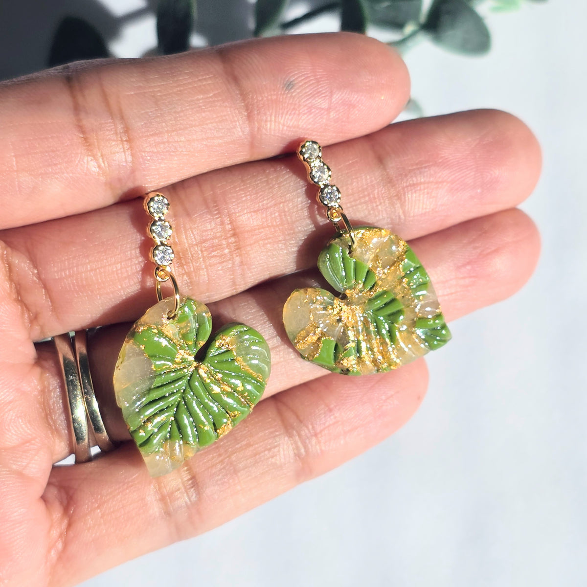 Green leaf-shaped earrings held in a hand with a light background