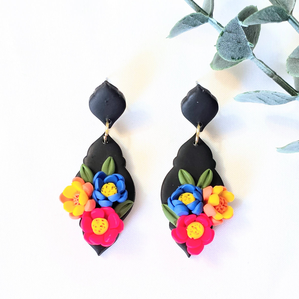 Colorful floral earrings on a white background with green leaves.