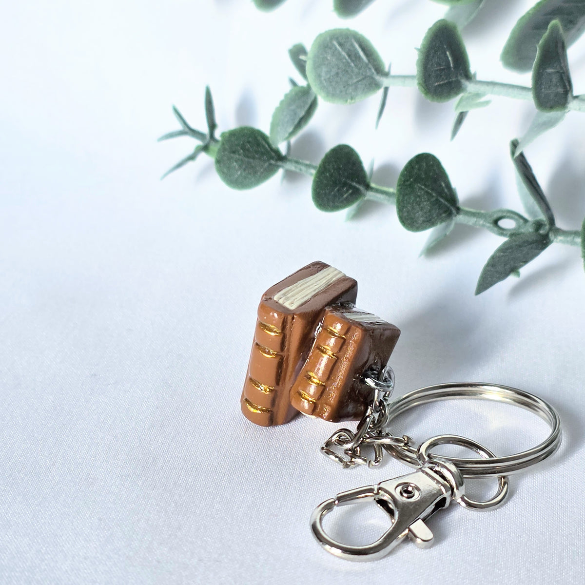 Book-shaped keychain on a white background with green leaves