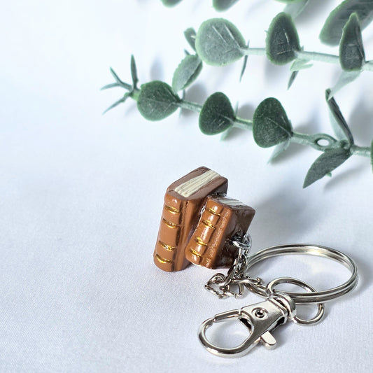 Book-shaped keychain on a white background with green leaves