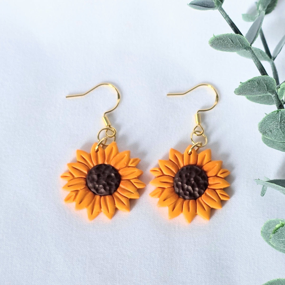Sunflower-shaped earrings on a white background with green leaves.