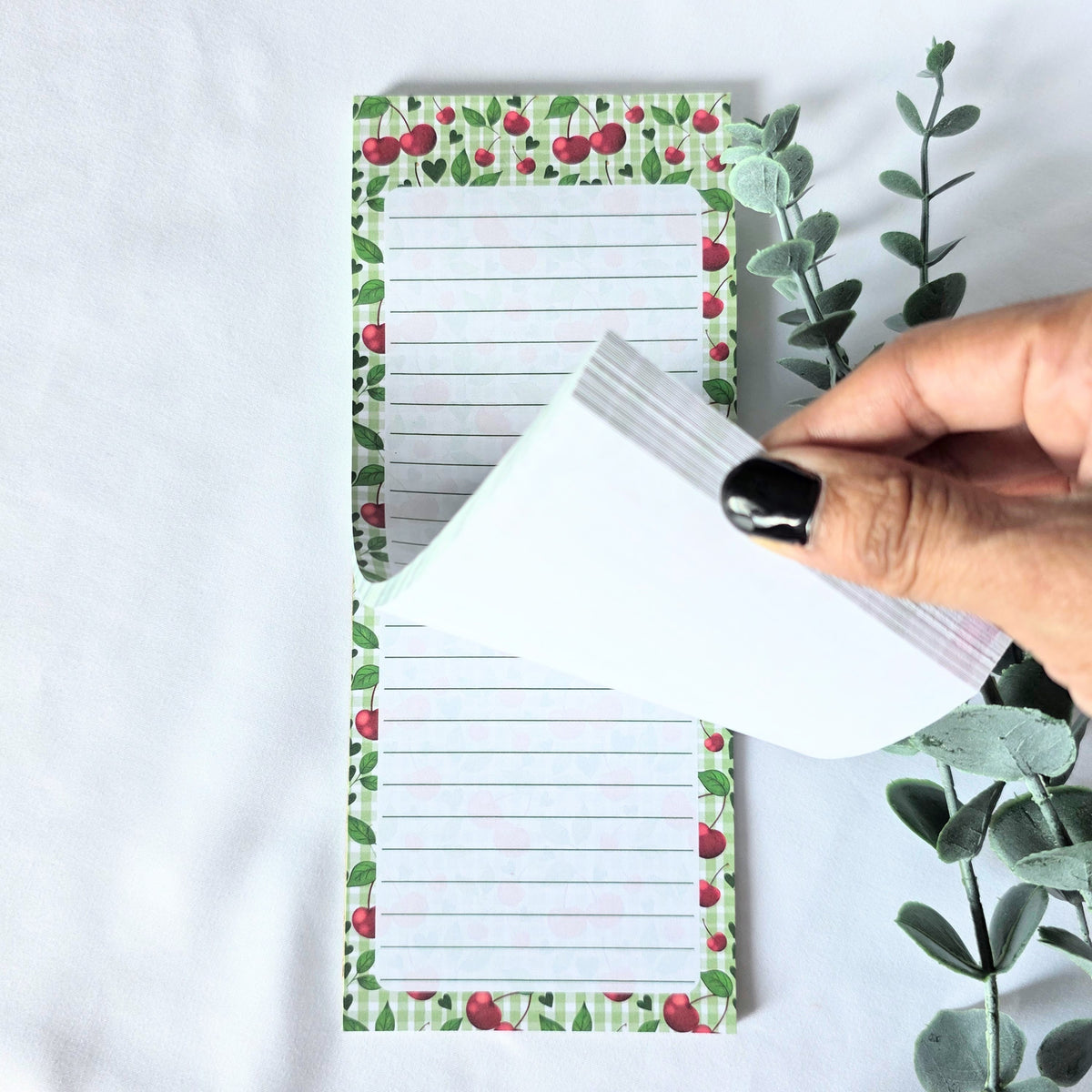 Notepad with cherry and leaf pattern held by a hand on a light background