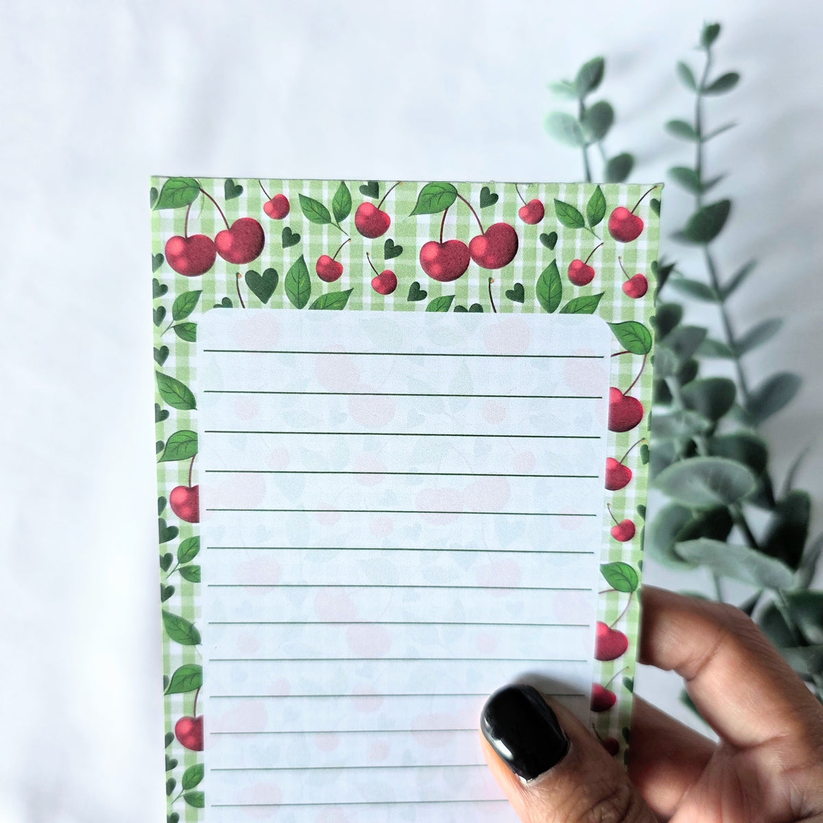 Notepad with cherry design held by a hand against a white background