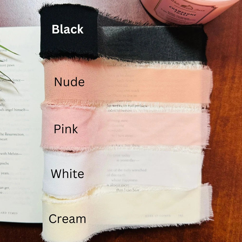 Color swatches of chiffon ribbon labeled Black, Nude, Pink, White, and Cream on a book with a plant in the background.