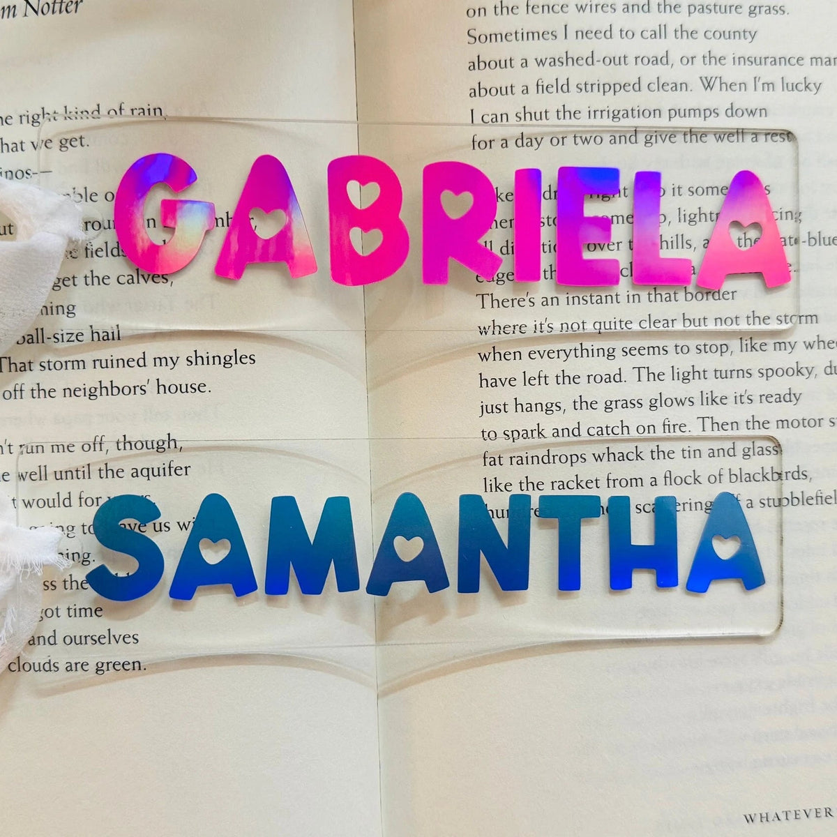Open book with colorful letters on an acrylic bookmark spelling 'Gabriela' and 'Samantha'