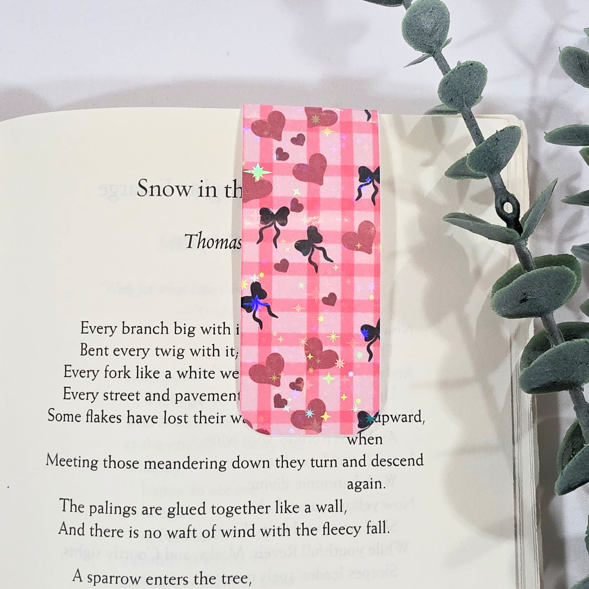 Pink checkered bookmark with heart and bow designs on a book page.
