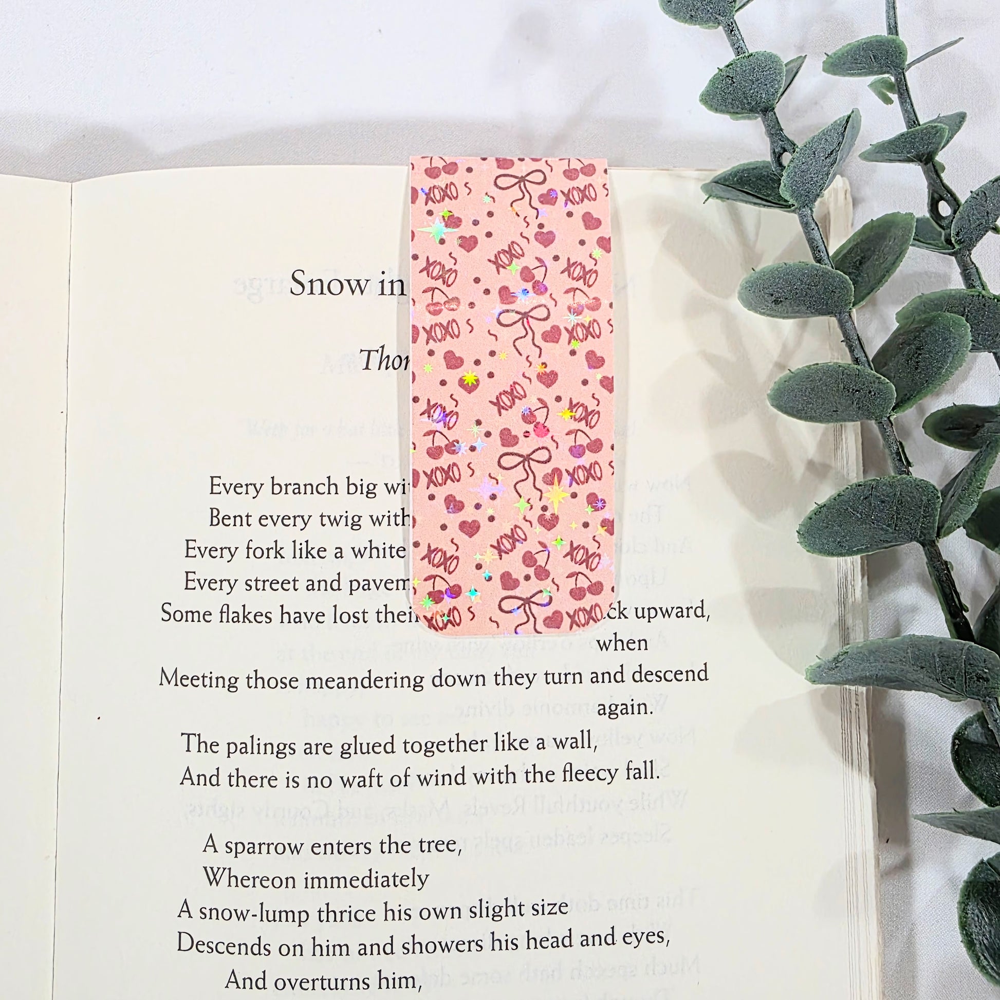 Open book with a decorative bookmark featuring hearts and bows, next to green leaves.