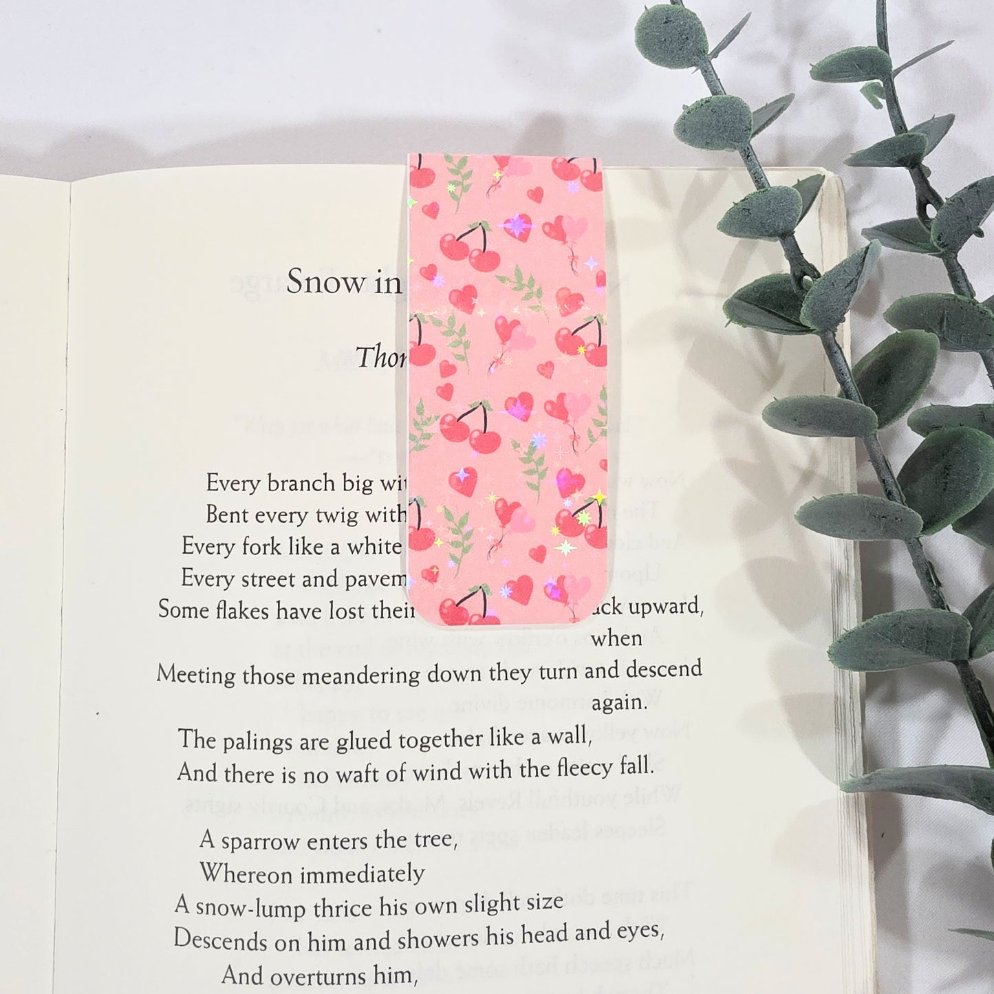 Book with a cherry-themed bookmark and a plant on a white background