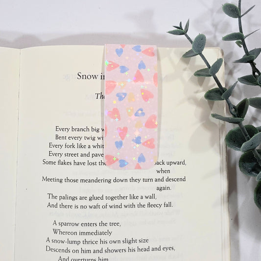 Open book with a colorful heart-patterned bookmark and a plant on a white background