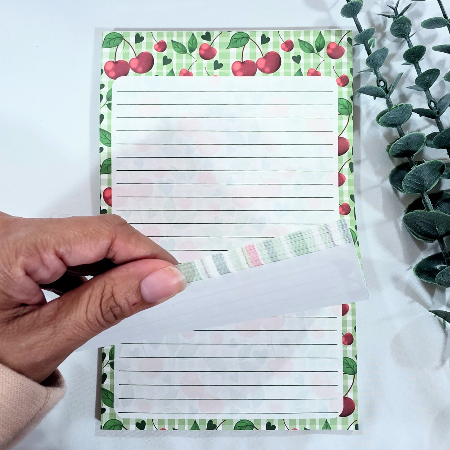 Notepad with cherry design held by a hand on a white background