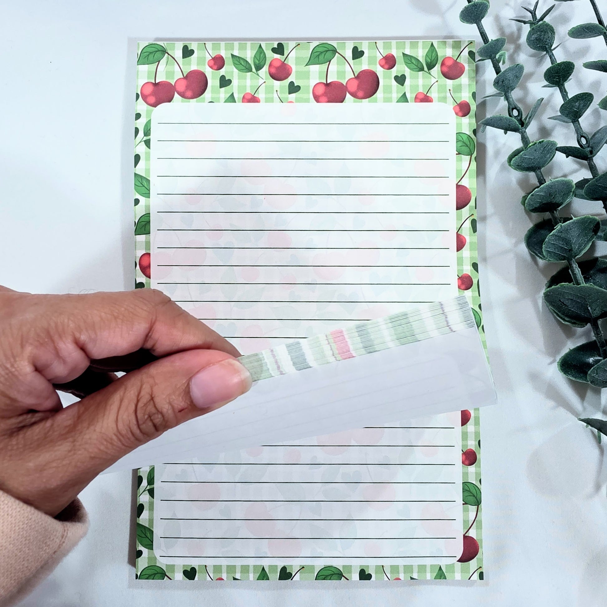 Notepad with cherry design held by a hand on a white background