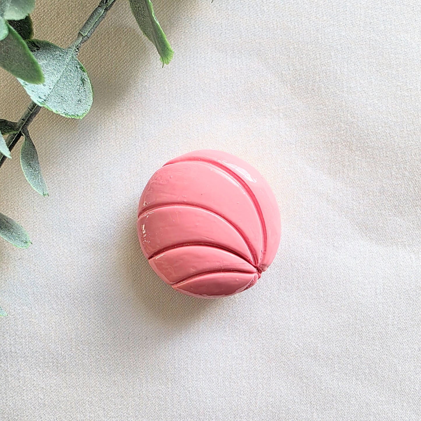 Pink conchita bread magnet on a light fabric background with green leaves.