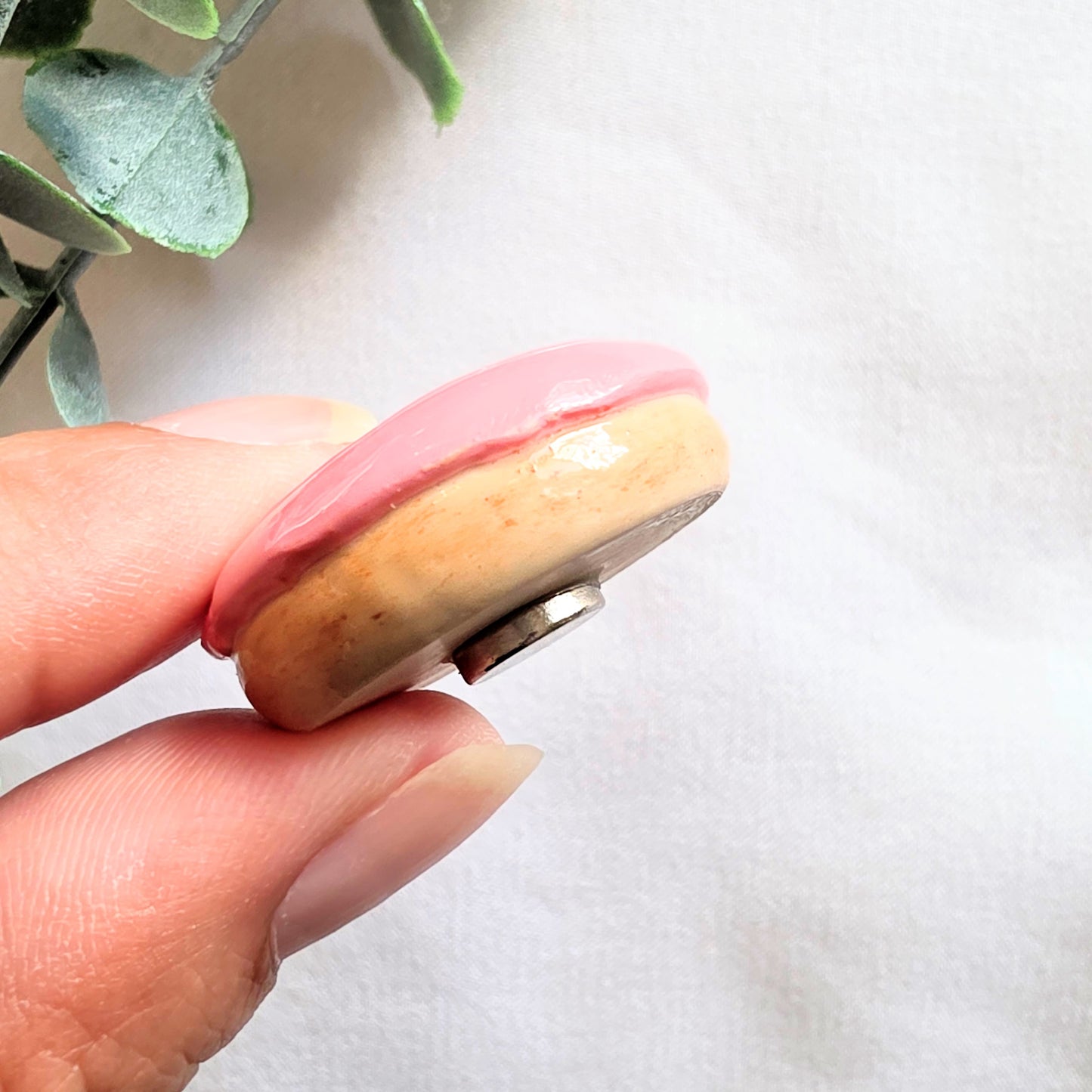Hand holding a round magnet with pink and beige colors on a white background