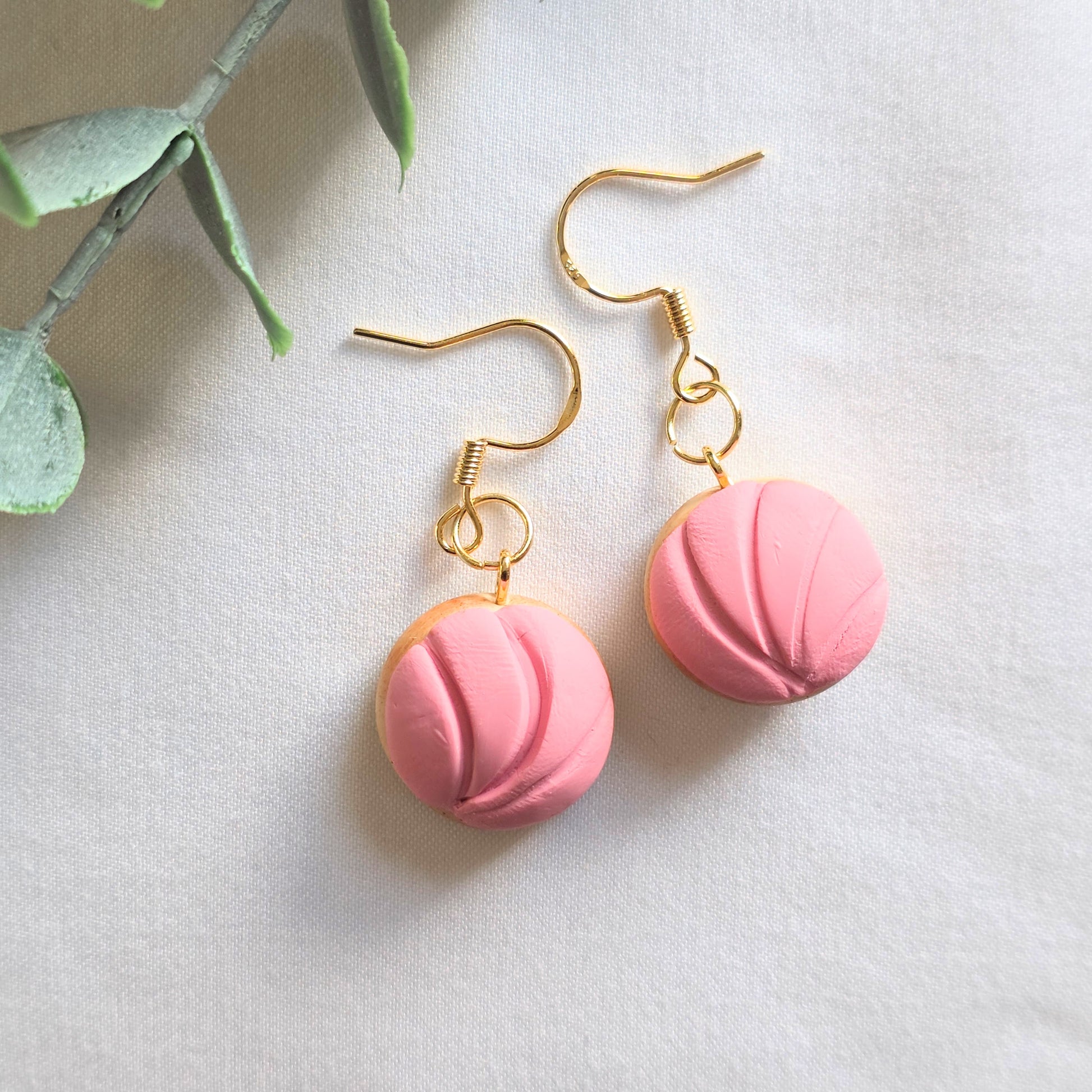Pink Conchita bread earrings with gold hooks on a light background. 
