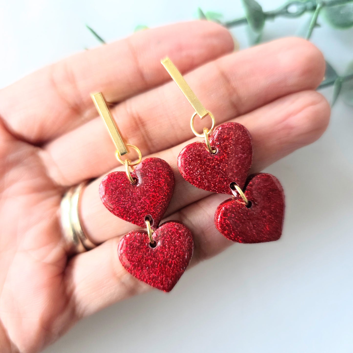 Red heart-shaped earrings with gold hooks held in a hand against a light background