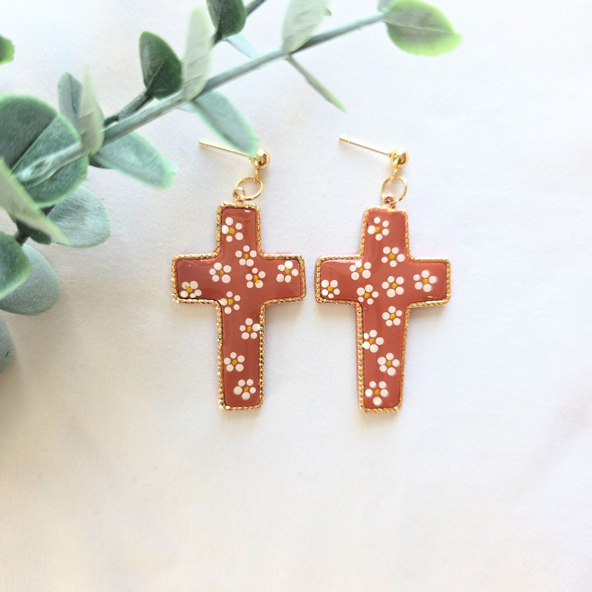 Handmade Mexican pottery–inspired cross earrings with gold plated brass, terracotta-colored polymer clay center, hand-painted white floral details, and 24k gold plated ball stud posts on a neutral background.