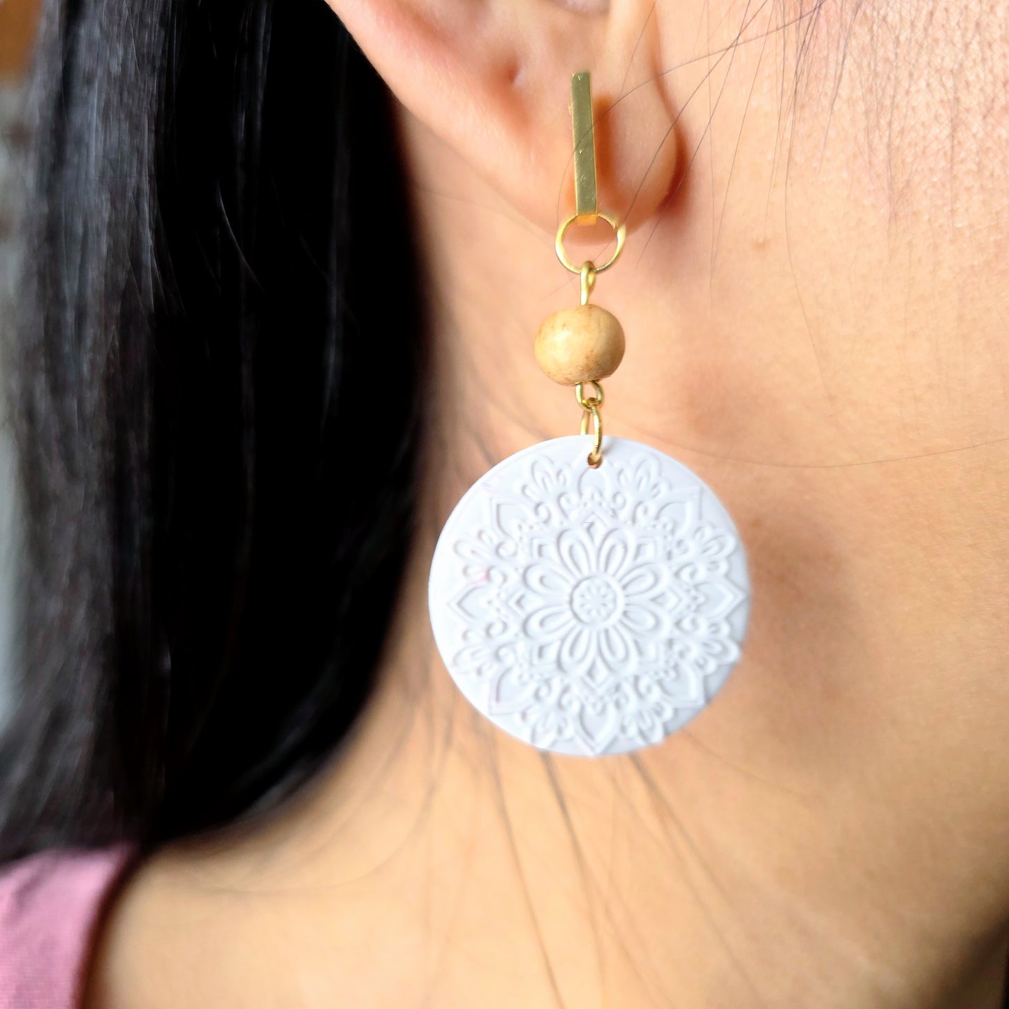 Close-up of a person wearing a white textured earring with a gold accent.