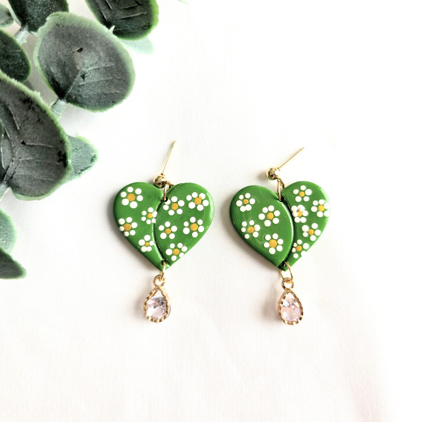 Green heart-shaped earrings with floral designs and teardrop charms on a white background.