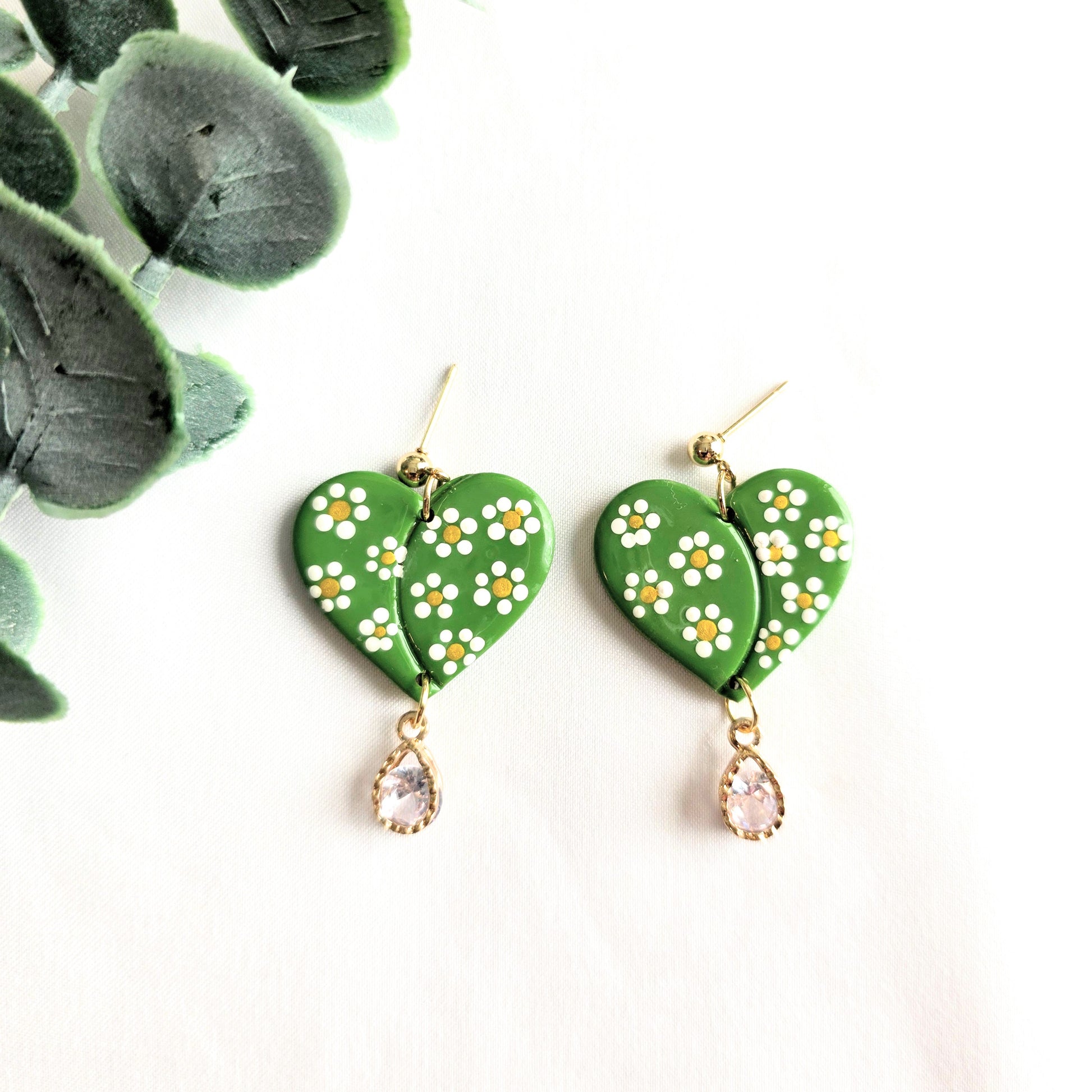 Green heart-shaped earrings with floral designs and teardrop charms on a white background.