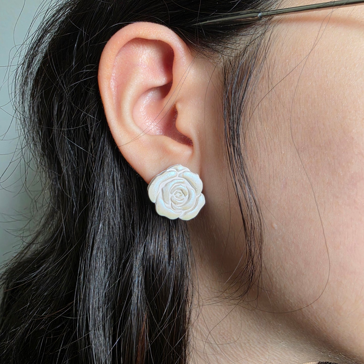 Close-up of an ear wearing a white floral earring with dark hair.