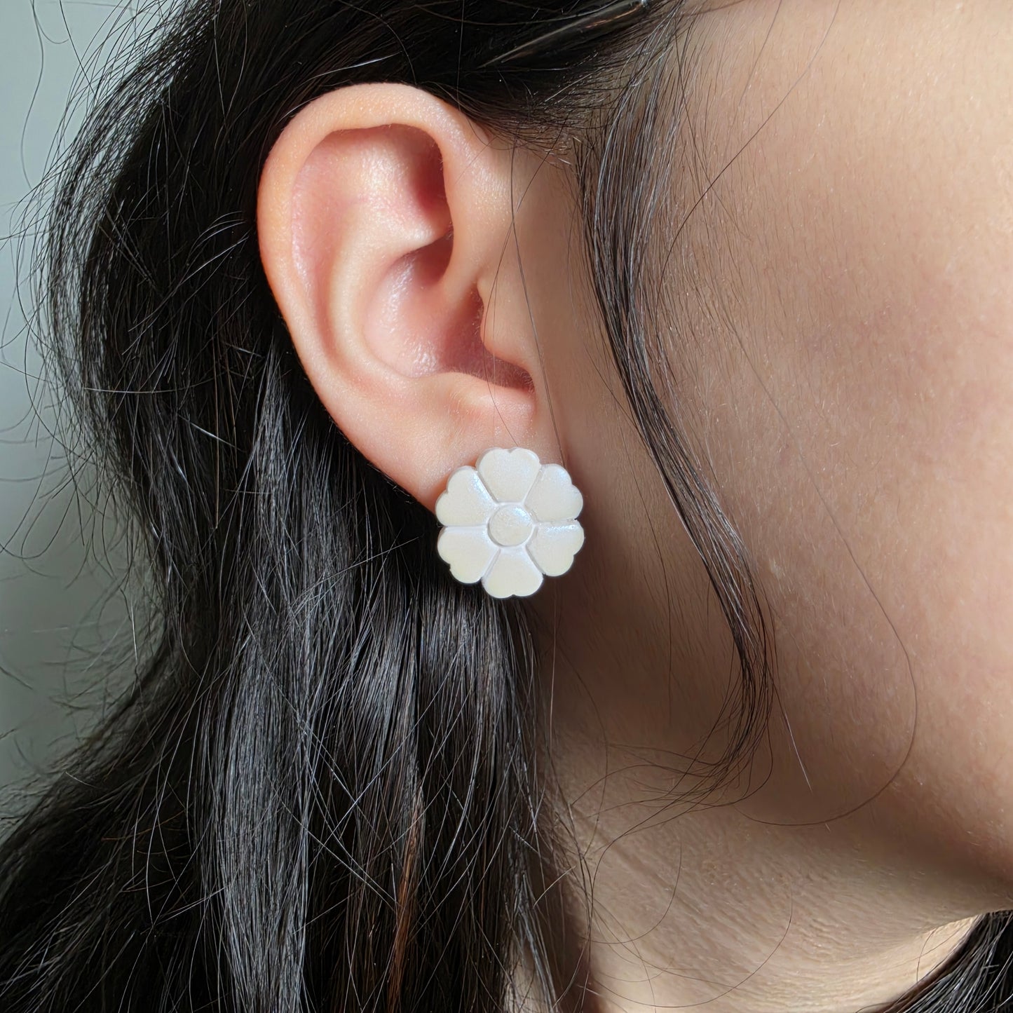 Close-up of an ear wearing a white flower-shaped earring with dark hair.