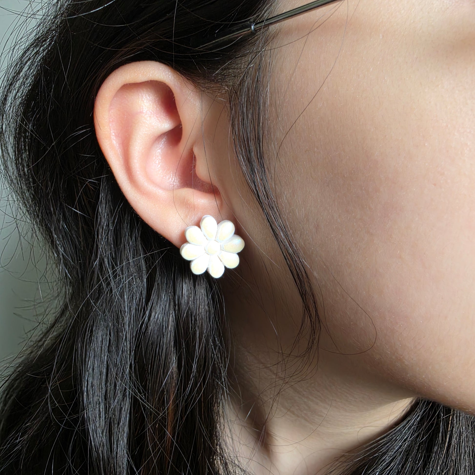 Close-up of an ear wearing a white flower-shaped earring with dark hair.