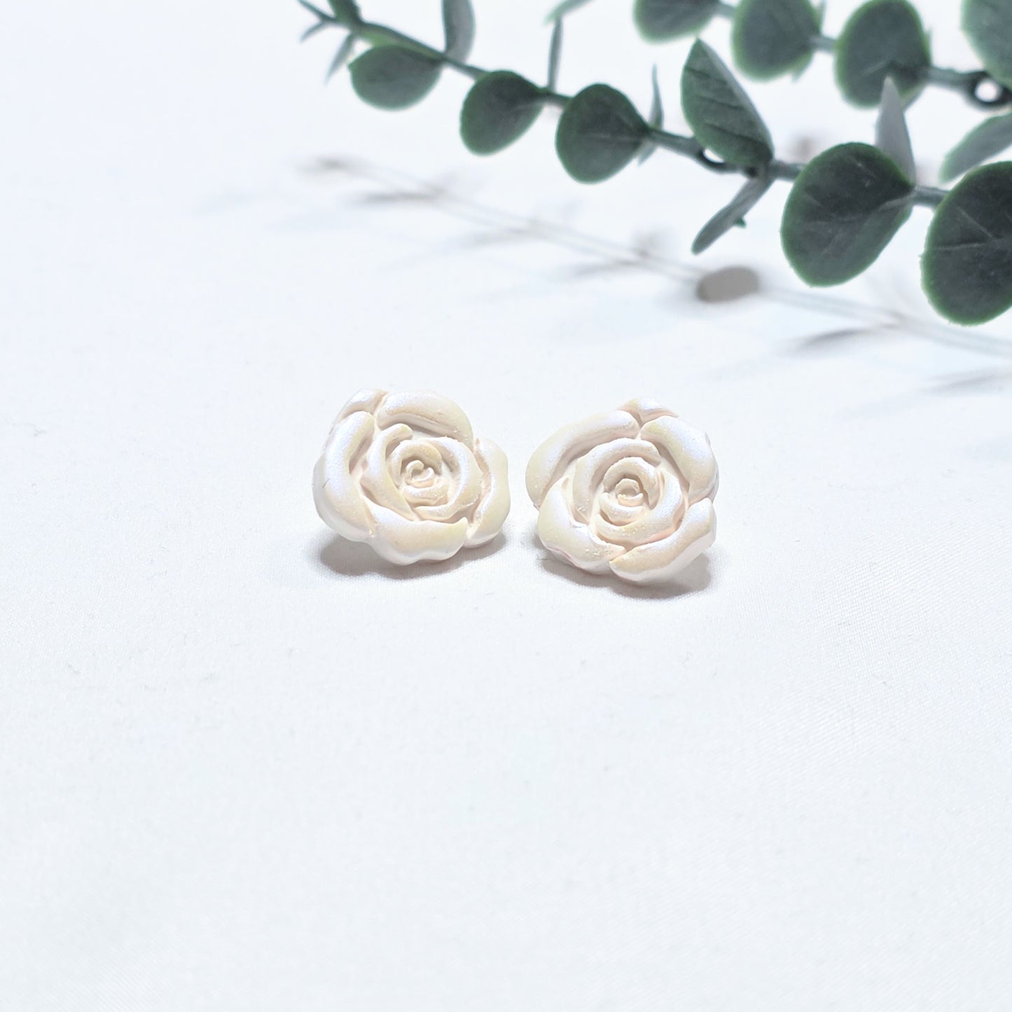 White rose-shaped earrings on a light white background with green leaves.