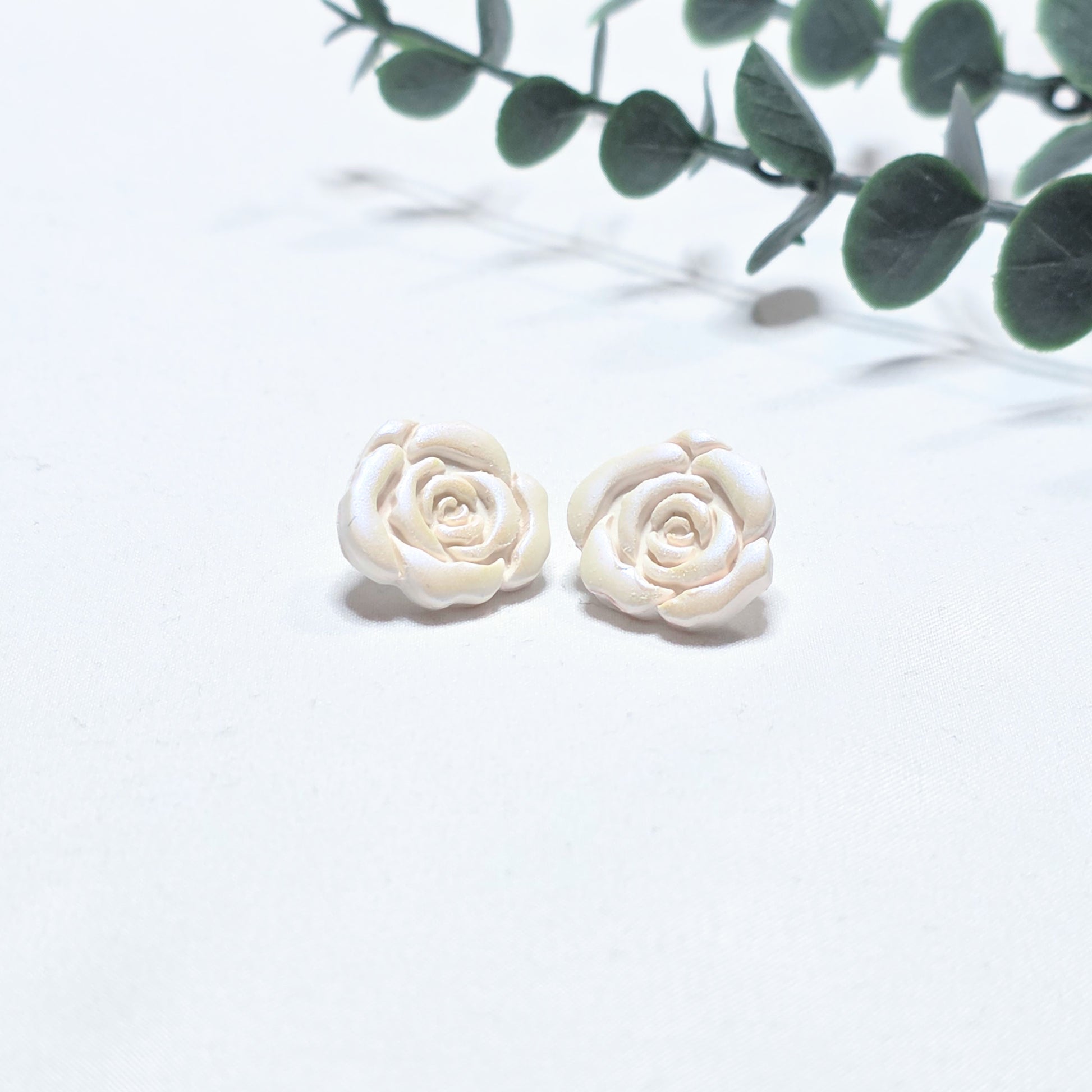 White rose-shaped earrings on a light white background with green leaves.