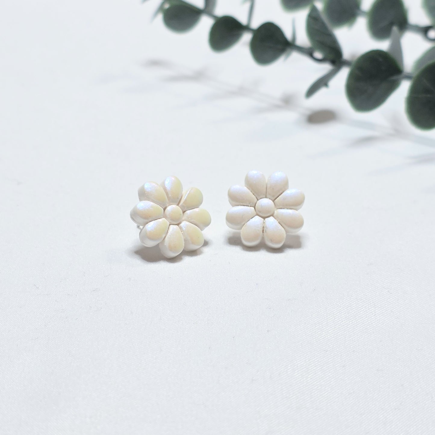 White flower-shaped earrings on a light background with green leaves.
