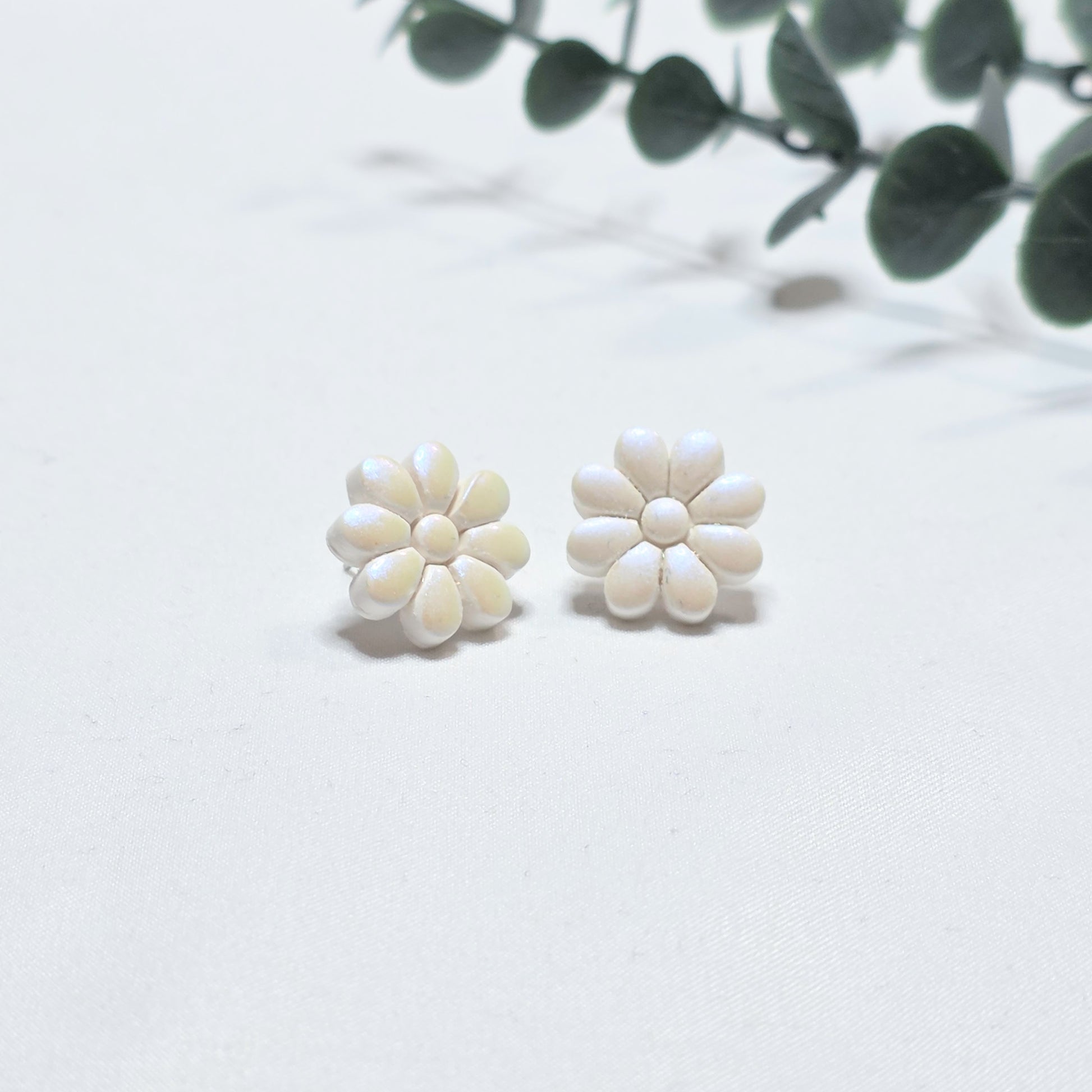 White flower-shaped earrings on a light background with green leaves.